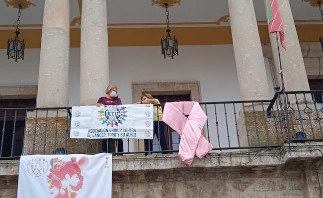 Dos mujeres toresanas, diagnosticadas de cáncer de mama, han sido las encargadas de colgar el lazo en el ayuntamiento
